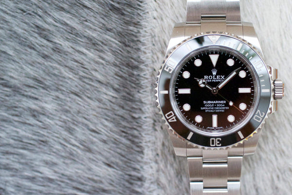 Stainless steel Rolex Submariner No Date luxury watch with black dial and bezel on textured surface