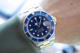 Close-up of a Rolex Submariner luxury watch with a blue bezel and two-tone gold and steel band.