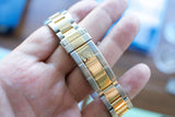 Close-up of a two-tone gold and stainless steel luxury watch bracelet held in a hand.