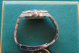 Side profile of a luxury gold and steel wristwatch with a blue bezel on a green leather surface