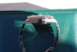 Close-up side view of a luxury Swiss watch with a gold fluted bezel on a teal background
