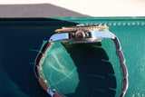 Side view of a luxury gold and steel watch with a metal link bracelet on a green surface.