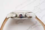 Side view of a luxury chronograph watch with a silver case and tan leather strap.