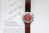 Sandoz luxury watch with a red dial and brown leather strap atop technical diagrams.