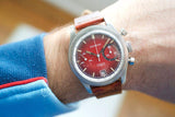 Close-up of a Sandoz vintage chronograph watch with a red dial and brown leather strap on a wrist