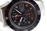 Black pilot chronograph watch with tritium markers, bold numerals, and stainless steel bracelet