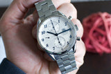 Silver chronograph wristwatch with blue hands and Arabic numerals on a wrist
