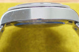 Close-up side view of a stainless steel watch case with minor scratches on a yellow surface
