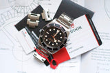 Stainless steel luxury dive watch with black bezel, warranty cards, and extra bracelet links