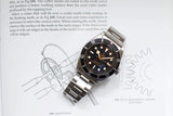 Stainless steel luxury dive watch with black bezel on open technical book with gear diagrams.