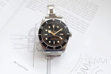Stainless steel automatic watch with black bezel and round markers on technical drawing background