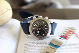 Luxury chronograph watch with a black dial and blue strap, displayed on an open book