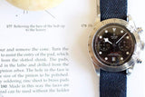 Stainless steel chronograph watch with black dial and denim strap on an open book