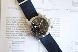 Luxury Swiss chronograph watch with black dial and fabric strap on an open book