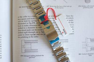 Stainless steel watch bracelet with tag and protective film placed on an open book