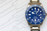 Blue Tudor Pelagos titanium dive watch with stainless steel bracelet on technical drawing background
