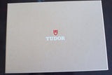 Textured beige box with red and white Tudor logo, luxury watch packaging