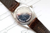 Close-up of a vintage watch caseback with engraved text, brown leather strap, silver case.