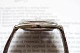 Side profile of a vintage stainless steel watch case with brown leather strap