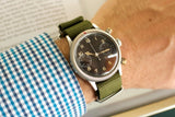 Vintage pilot watch with black dial and olive NATO strap on wrist