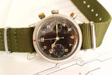Vintage pilot chronograph watch with black dial and olive green NATO strap on schematic paper