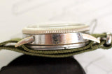 Side view of vintage pilot watch case with visible wear and green fabric strap