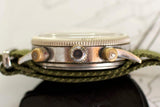 Close-up side view of vintage pilot's watch case with bronze pushers and green fabric strap