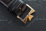 Close-up of a gold-tone buckle on a brown leather luxury watch strap