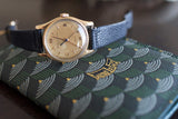 Vintage Swiss gold watch with black leather strap on patterned green wallet