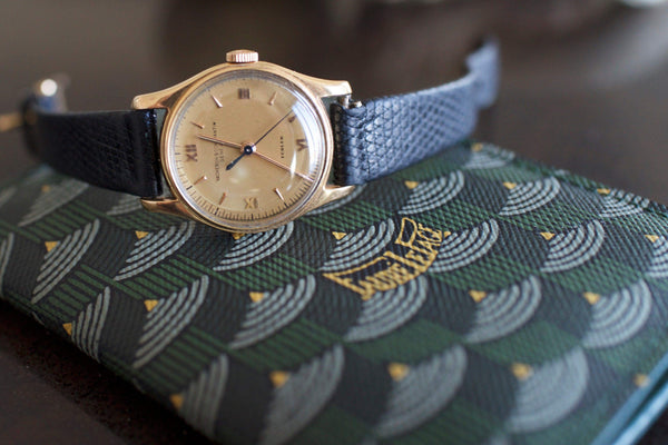 Vintage Swiss gold watch with black leather strap on patterned green wallet