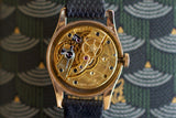 Vintage Swiss luxury watch with exposed gold mechanical movement and black textured strap