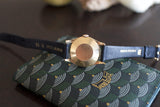 Gold luxury Swiss-made wristwatch with blue leather strap, caseback view on patterned wallet