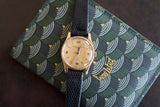 Vintage gold wristwatch with black leather strap on patterned green case