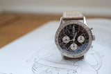 Vintage black dial chronograph watch with beige strap on technical drawing background