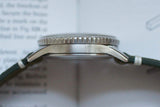 Side view of a vintage stainless steel luxury watch with green strap on open book