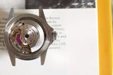 Close-up of mechanical watch movement with exposed gears and rotor on open book