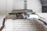 Side view of vintage stainless steel luxury watch case and crown with screw-down logo