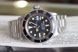 Vintage stainless steel diver watch with black dial and date window, placed on an open book