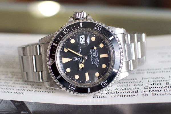 Vintage stainless steel diver watch with black dial and date window, placed on an open book