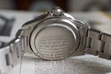 Close-up of stainless steel vintage wristwatch caseback, bracelet visible, placed on an open book