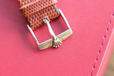 Close-up of a silver buckle on a brown textured leather watch strap against a red background
