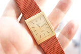 Close-up of a gold Rolex Cellini square face watch with a brown textured leather strap.